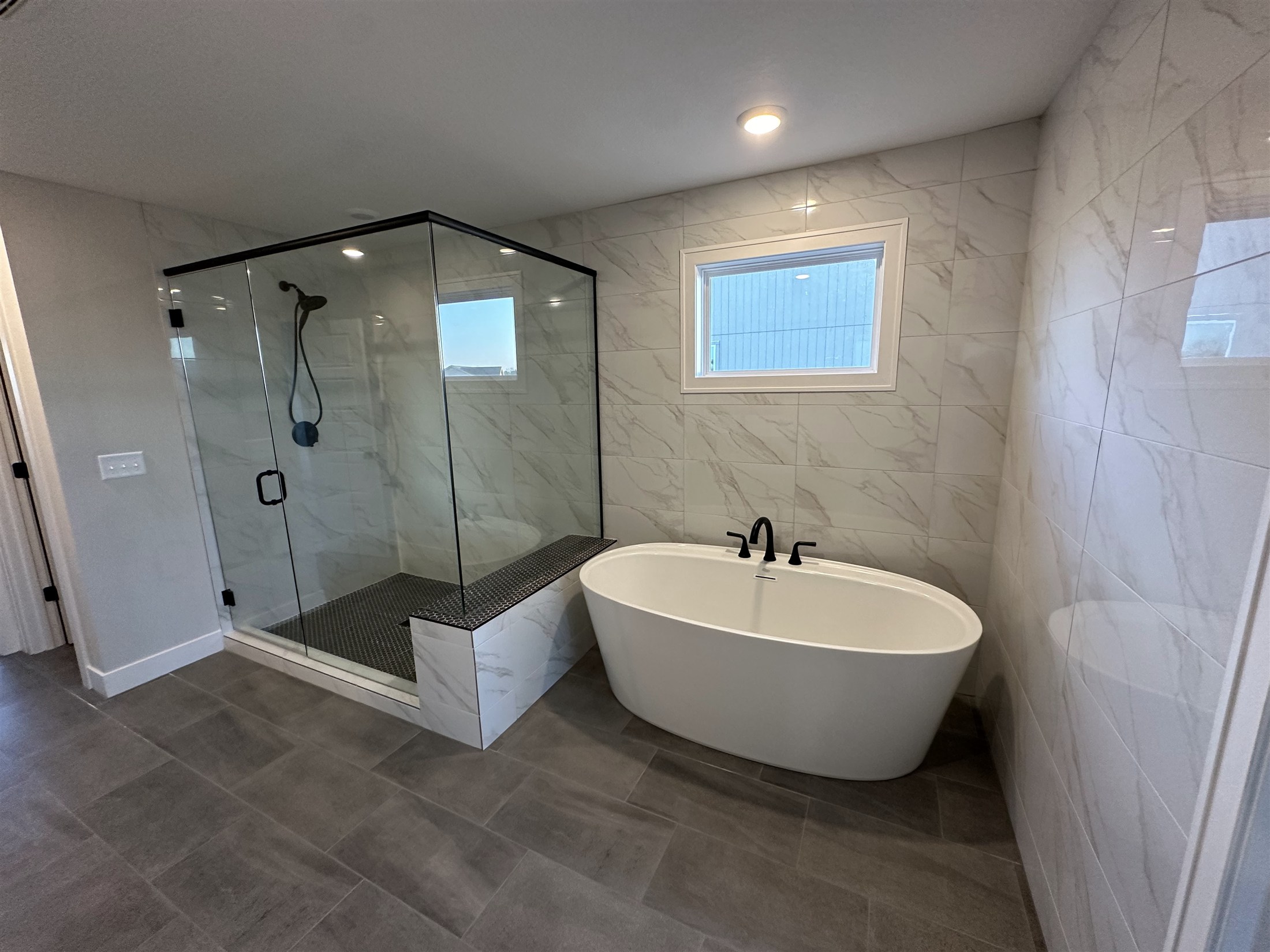 Heartland Tile bathroom installation with a glass walk-in shower, freestanding bathtub and large-format tile